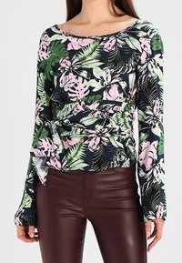 Haut à manches longues avec un motif floral dans les tons de bleu foncé, vert et rose. Présente une taille cintrée et un décolleté large ; texture de tissu lisse.