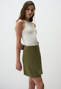 Top en rib blanc associé à une jupe verte olive longueur genoux avec une texture subtile et un design simple.