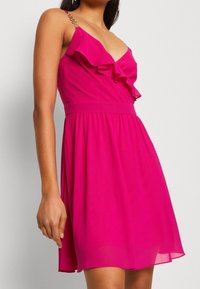 Fuksjowa sukienka z frędzlowym dekoltem, regulowanymi ramiączkami z łańcuszkami oraz elastycznym paskiem w lekko opadającym materiale.