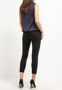 Satin navy sleeveless top paired with fitted black pants, featuring a smooth texture and ankle-length design, complemented by high heels.