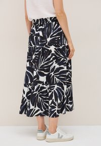 Jupe maxi à volants en noir et blanc avec un motif de feuilles, fabriquée en tissu léger. Portée avec des baskets blanches avec des accents gris.