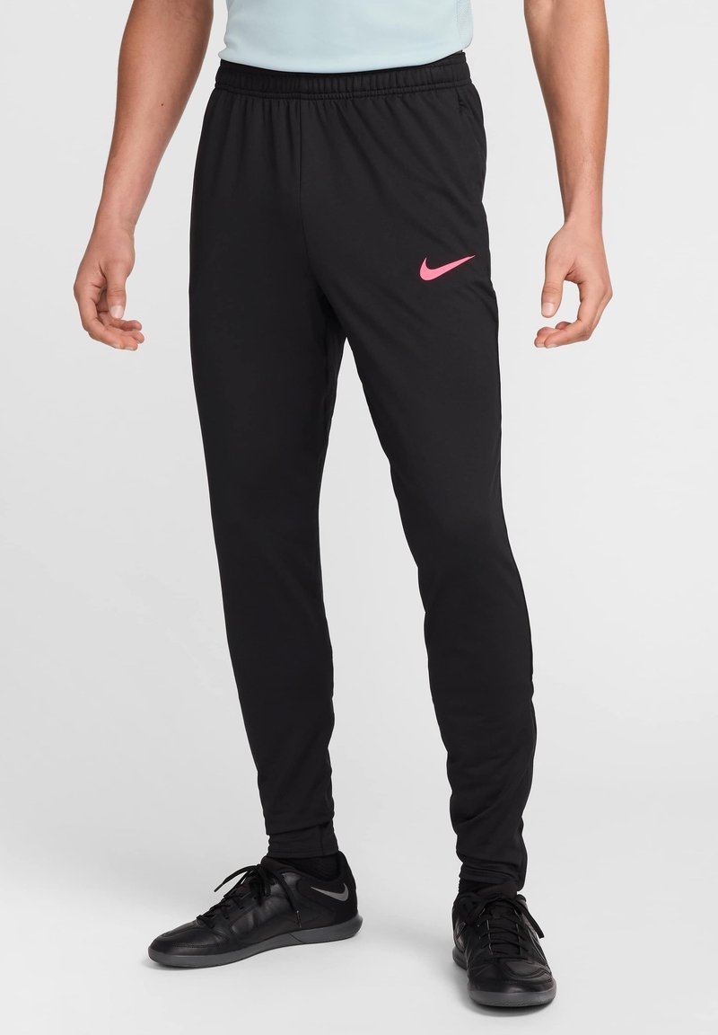 Juodos sportinės kelnės su elastinga juosta, ant kairiojo kojos turi rožinį Nike logotipą ir siaurėjantį siluetą. Medžiaga atrodo lygi ir lengva.