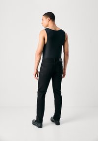 Top sin mangas negro de canalé combinado con jeans negros de corte recto. Los zapatos del modelo son mocasines negros con un diseño texturizado.
