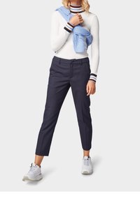 Granatowe spodnie w kratkę o dopasowanym kroju, zestawione z białą bluzką z długim rękawem w paski oraz jasnoniebieskim swetrem dzianinowym zarzuconym na ramiona.