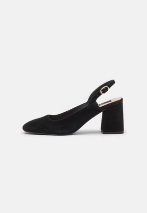 Czarny zamszowy damski but typu slingback z blokowym obcasem i paskiem na złotą klamrę na jednolitym jasnym tle.