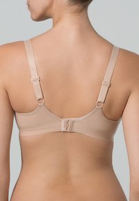 Soutien-gorge sans fil beige avec bretelles réglables, fermeture à crochets et œillets, tissu lisse et design sans couture à l'arrière.