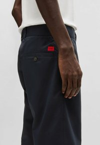 Marina tygbyxor med en mjuk struktur; har en röd etikett med "HUGO" och en knappad bakficka; slim-fit design.