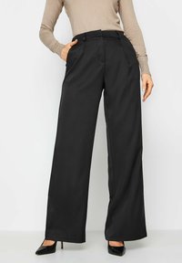 Zwarte wijde broek met een gladde textuur, voorzien van een middelhoge taille en zijzakken, gecombineerd met zwarte pumps met puntige neuzen.