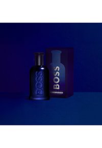 Tummansininen hajustepullo, jossa "BOSS" kohokuvioitu edessä, seisoo vierekkäin vastaavan laatikon kanssa, jossa lukee "BOSS Bottled Night Eau de Toilette."