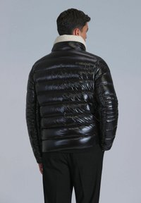 Black puffer jacket with a shiny finish, quilted design, and a cream shearling collar, seen from the back. Stylish fit, no visible hardware.