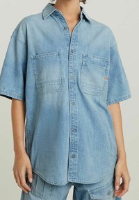 Ljusblå denimskjorta med avslappnad passform, korta ärmar, två framfickor och knäppning framtill. Mjuk textur och avslappnad design.