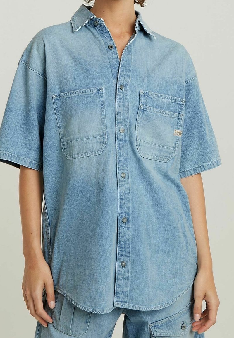 Ljusblå denimskjorta med avslappnad passform, korta ärmar, två framfickor och knäppning framtill. Mjuk textur och avslappnad design.