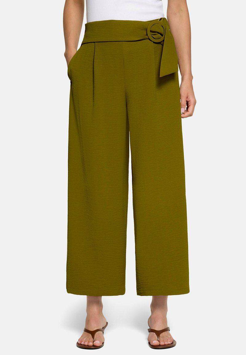 Pantalon à jambes larges vert olive taille haute, poches latérales et ceinture en tissu avec boucle circulaire porté par une personne en sandales marron.