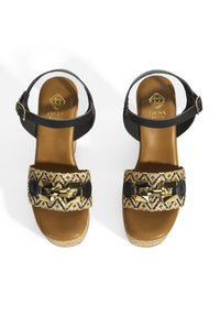 Sandales noires et marron avec une lanière tressée ornée d'accents géométriques dorés. Semelle intermédiaire en liège avec un coussin de pied doré texturé. Lanière de cheville réglable.
