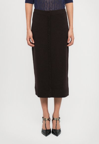 Jupe midi en tricot marron à finition unie, avec une fermeture boutonnée à l'avant et une ceinture côtelée. Associée à des talons noirs pointus.