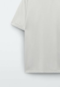 Hellgraues T-Shirt mit kurzen Ärmeln, aus weichem Stoff gefertigt, mit entspanntem Schnitt und glatter Textur, mit einfachen, klaren Linien.