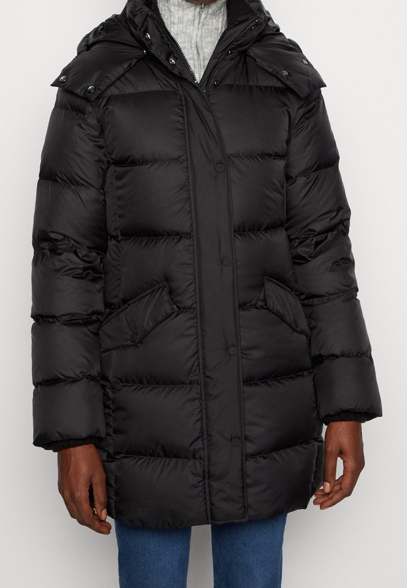 Zwarte pufferjas met een capuchon, uitgerust met drukknoopsluiting, opgestikte zakken en een gewatteerd ontwerp voor warmte en isolatie. Zachte textuur.