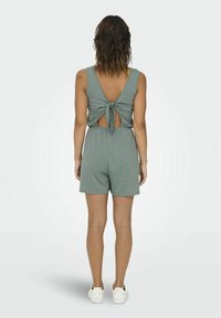 Grijze mouwloze romper met een V-rug, geknoopte strikdetail en uitsnijding op de rug. Heeft een relaxte pasvorm en een korte zoom.