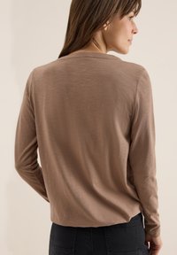 Chemise à manches longues en tissu taupe doux avec une coupe décontractée. Dotée d'un col rond et d'une texture lisse, elle est associée à un pantalon sombre.