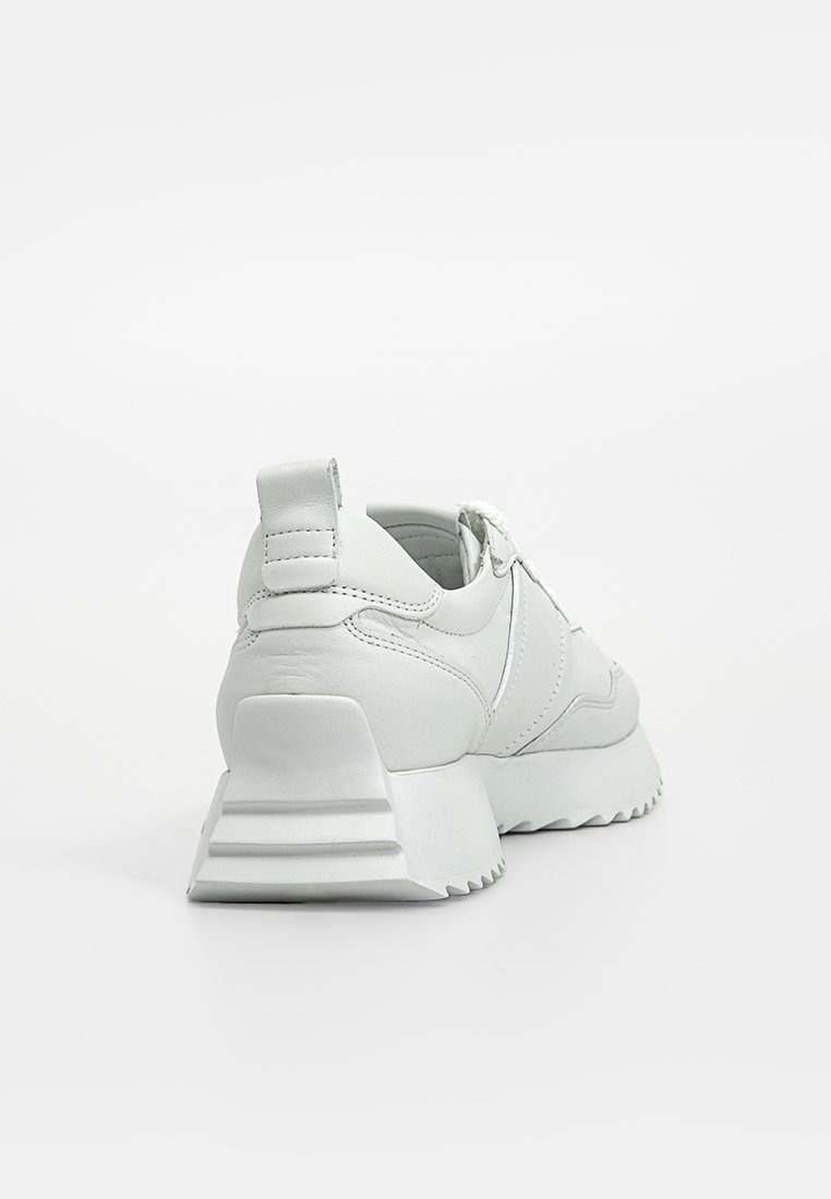 Weißer Ledersneaker mit dickem, geriffelten Sohle und Fersenschlaufe, von hinten auf einem weißen Hintergrund betrachtet.