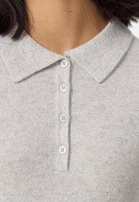 Jasnoszara koszulka polo wykonana z miękkiej dzianiny. Posiada klasyczny kołnierzyk, pięć białych guzików z przodu oraz subtelne logo na piersi.