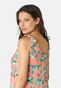 Abito senza maniche floreale in corallo, con foglie tropicali verdi e fiori rosa. Laccetti sulle spalle e design a V sul retro con dettagli a bottone.