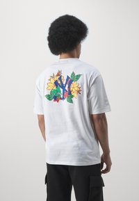 Camiseta de algodón blanca de manga corta con un gráfico floral colorido de flores amarillas, hojas verdes y acentos azules en la parte posterior.