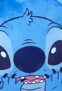 Gros plan d'un personnage de dessin animé bleu avec de grands yeux, un gros nez noir, des dents acérées et de petites griffes près de sa bouche.