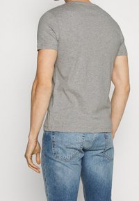 Graues Kurzarm-T-Shirt aus Baumwolle. Mit Rundhalsausschnitt und slim fit, kombiniert mit blauen Jeans.