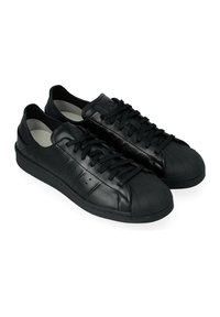 Un paio di sneaker in pelle nere a taglio basso con punta in gomma, chiusura con lacci e accenti laterali perforati su sfondo bianco.