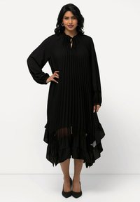Vestido midi negro con plisado, cuello redondo, detalle de lazo, mangas largas y dobladillo con volantes en capas. Tejido ligero con una textura suave.