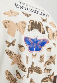 Bavlněné tričko s bílým pozadím, na kterém jsou různé ilustrované motýly a můry v tlumených hnědých barvách a živá modrá a červená můra.