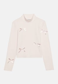 Langermet topp laget av ribbet stoff i lys rosa, med multiple satengsløyfer sydd på fronten og ermene. Høy mock neck design.