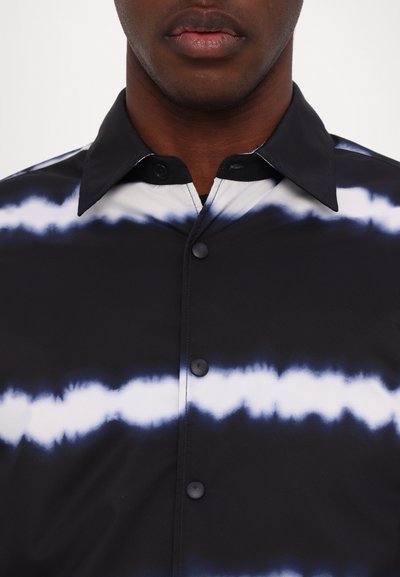 Sort skjorte med et tie-dye mønster, der har vandrette hvide og blå striber, en klassisk krave og sorte knapper. Glat stofoverflade.