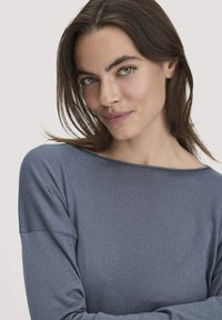 Langärmliges Oberteil aus weichem, geripptem Stoff. Verfügt über einen Bootsausschnitt und eine gedämpfte blaue Farbe. Glatte Textur mit engen Ärmeln.