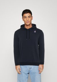 Felpa blu navy con coulisse, orlo e polsini a coste. Presenta un piccolo logo rosso e blu sul petto. Realizzata in tessuto morbido e strutturato.