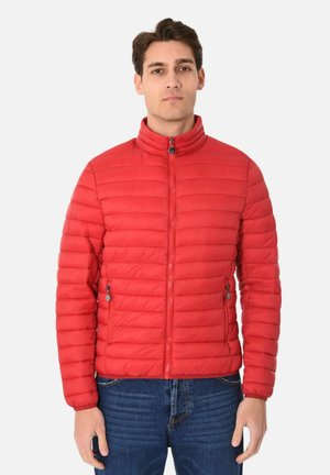 Giacca isolata rossa con colletto alto, design a righe verticali, polsini elastici e tasche laterali con cerniera. Indossata sopra jeans blu.