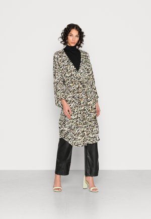 Μακριά, μοτίβο ρομπ κατά το πολυχρωμο σχέδιο με μαύρους, λευκούς και πράσινους τόνους, σε συνδυασμό με μαύρους δερμάτινους παντελόνες και ανοιχτοπράσινα τακούνια.