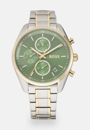 Grünes Zifferblatt Hugo Boss Uhr mit goldenen Akzenten, drei Subzifferblätter für 24-Stunden-Zeit und Tage, gold- und silberfarbenes Metallarmband, Datumsanzeige bei 4 Uhr.