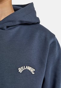 Felpa blu navy con una texture morbida. Presenta un collo rotondo e un logo del marchio ricamato bianco sul petto.