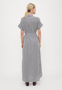 Vestido maxi listrado em azul-marinho e branco, com mangas curtas e esvoaçantes, cintura ajustada e uma saia longa e fluida. Textura de tecido suave.