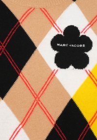 Maglione a maglia in beige, nero, bianco e giallo con motivo a rombi, caratterizzato da linee diagonali rosse e un logo a fiore nero con la scritta "Marc Jacobs."