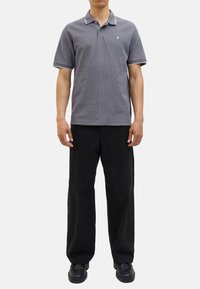 Camisa polo a rayas grises con cuellos y puños blancos, combinada con pantalones de pierna ancha negros y zapatos negros. Atuendo casual en una figura de pie.