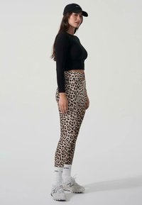 Leggings s uzorkom leoparda napravljeni od rastezljivog materijala, upareni s crnom majicom dugih rukava i crnom kapom. Bijele sportske čarape i sive tenisice.