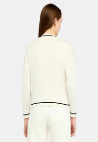 Cardigan crema con bordi neri, maniche lunghe e vestibilità rilassata. Tessuto liscio, colore solido, senza motivi. Vista mostra il design posteriore.