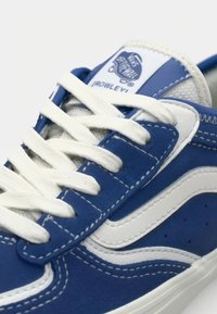 Blue suede sneaker with white leather accents and laces. Features a stitched design and branding on the tongue. Streamlined shape.