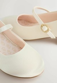 Balerini albi cu textură netedă, vârf rotund și curea la gleznă prevăzută cu o cataramă accentuată cu aur. Căptușeală roz pal cu model floral.