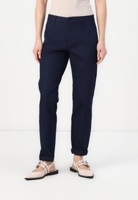 Granatowe spodnie na miarę o prostym kroju, z zapięciem na guzik i podwiniętymi mankietami. Materiał wygląda na gładki i lekki.