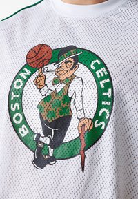 Camiseta de baloncesto de malla blanca con el logo de los Boston Celtics en verde y negro, que representa a un duende sosteniendo un balón de baloncesto y un bastón.