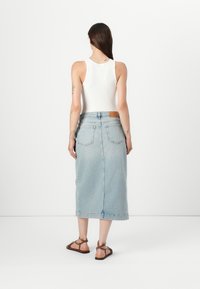Lys blå denim midi skjørt med rett snitt, fem lommer, og en brun lærmerke på midjebandet, kombinert med brune sandaler.